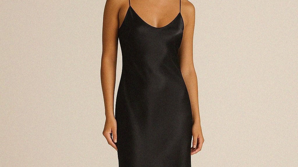 Woman wearing a black bias cut silk slip dress on beige background. 