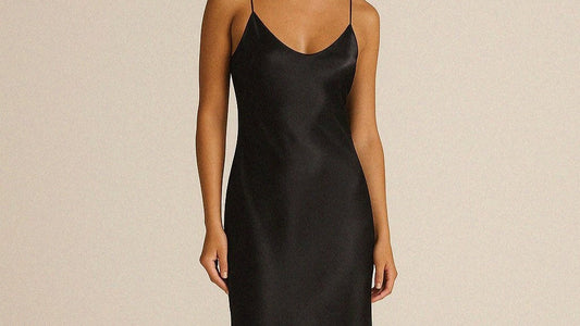 Woman wearing a black bias cut silk slip dress on beige background. 