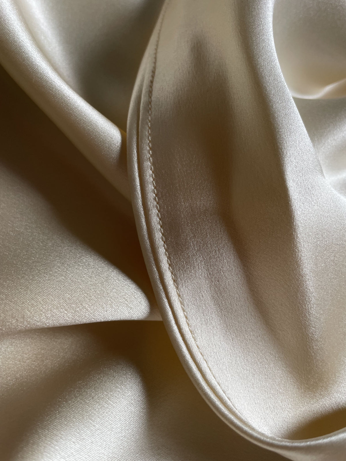 Close-up of champagne bias cut silk slip dress hem.