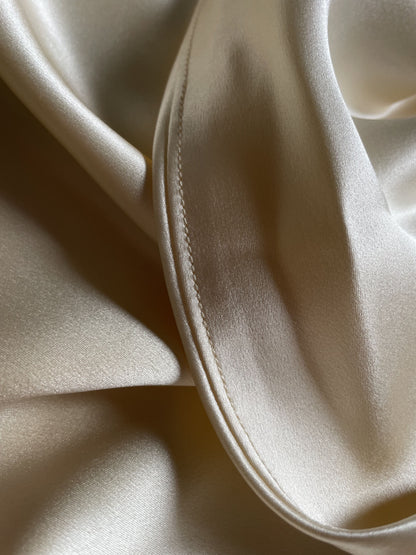 Close-up of champagne bias cut silk slip dress hem.