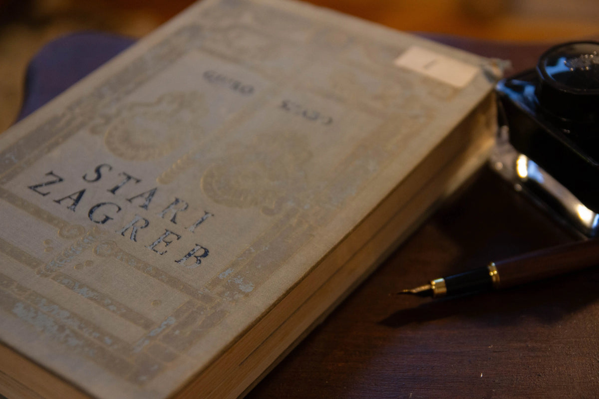 A vintage-style book with the title 'STARI ZAGREB' on the cover, photographed on a wooden surface next to a fountain pen and.