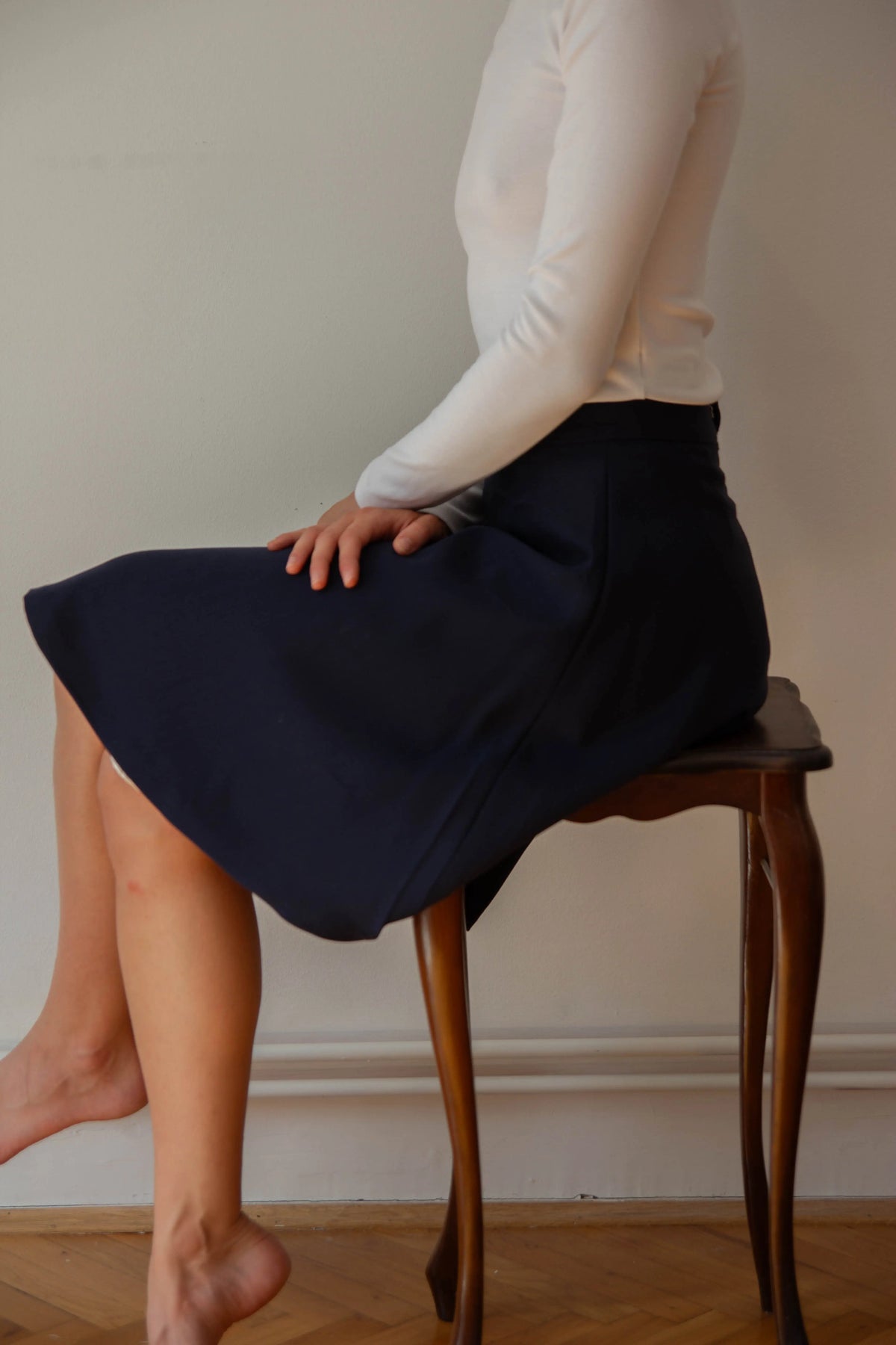 A well dressed woman sitting tall on wooden table, wearing a midnight blue wool skirt and a white shirt.
